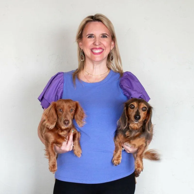 confident middle-aged white woman with blond hair smiling and holding two small dogs