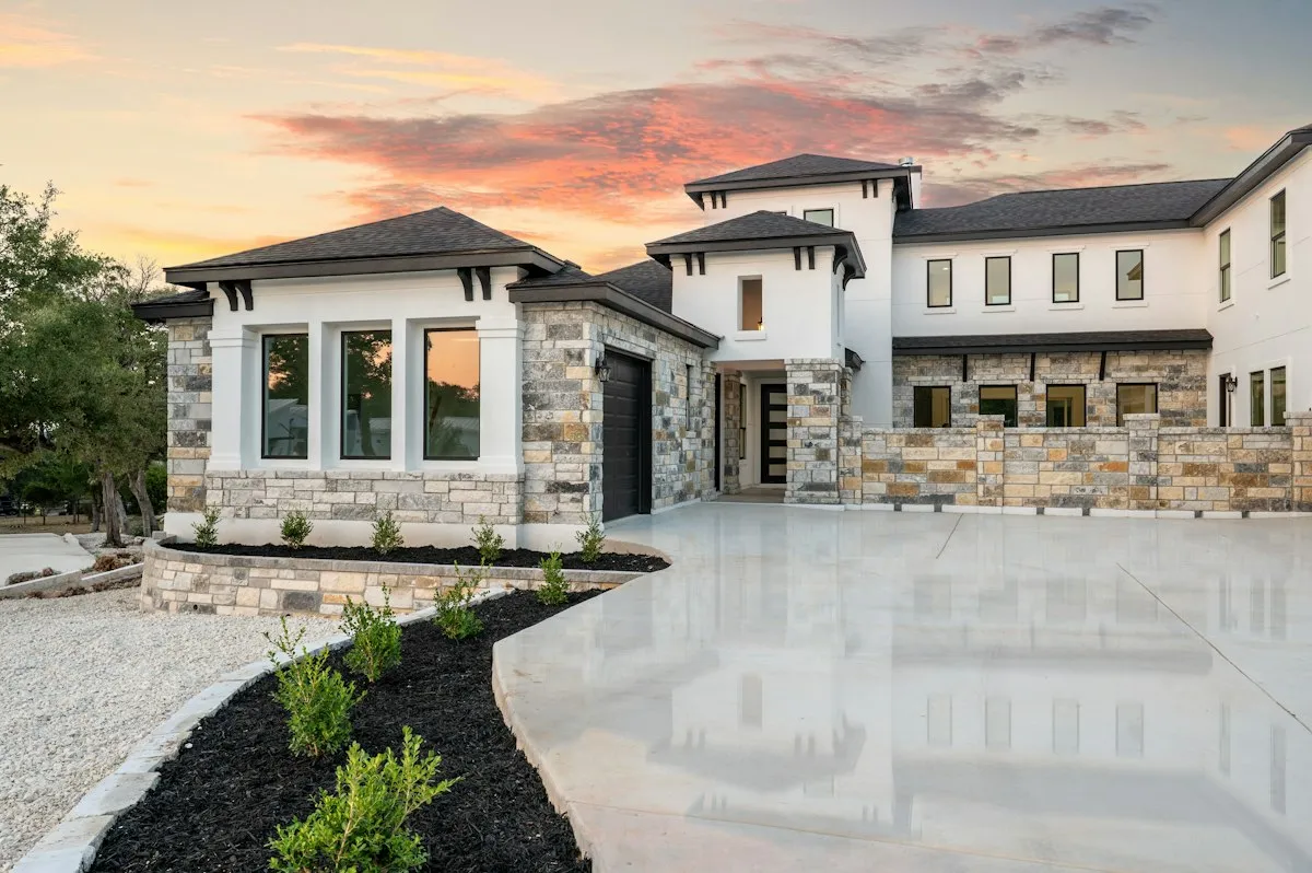 Modern Hill Country custom home with stone and stucco exterior lit at sunset, front entrance and driveway