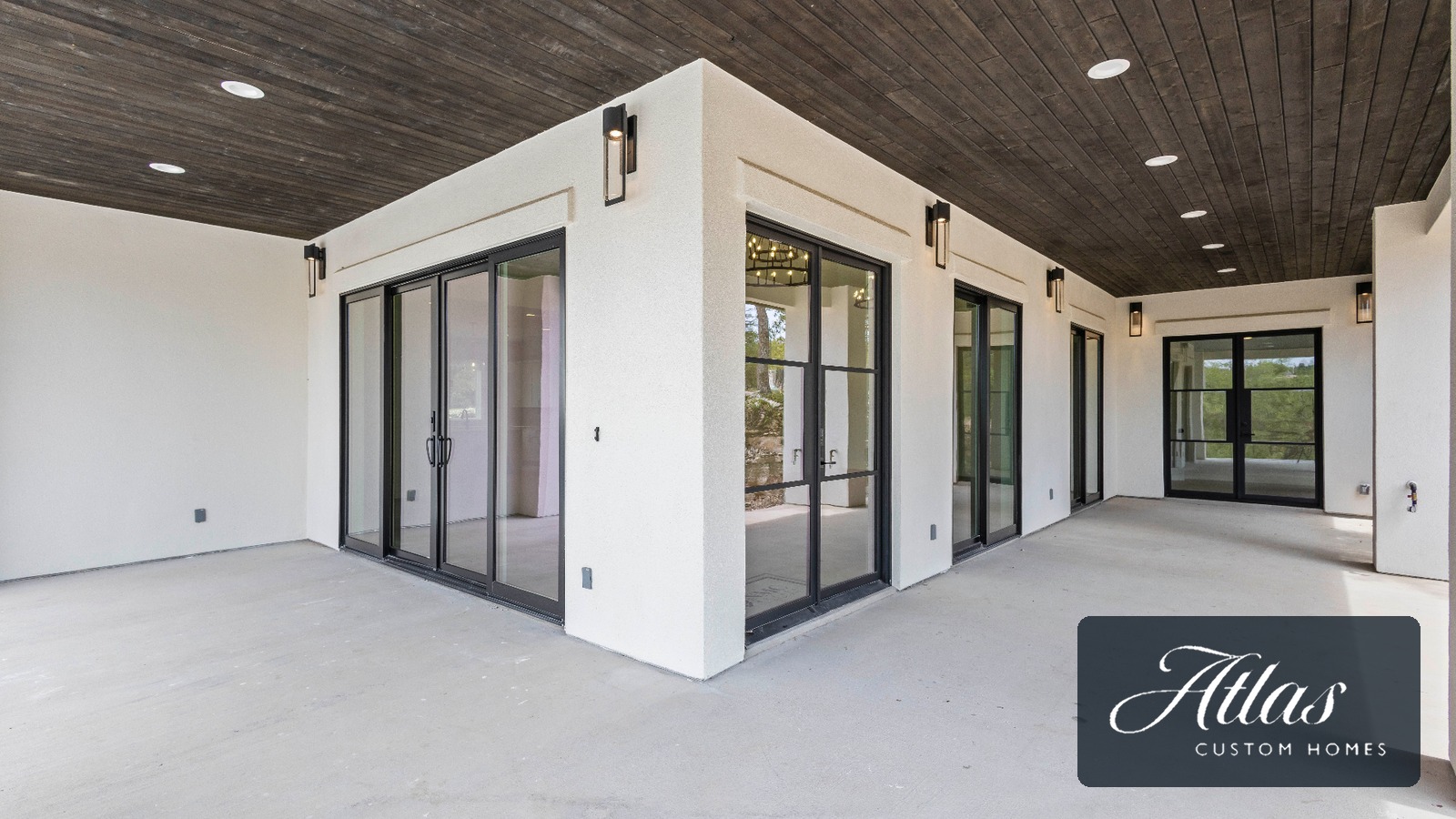 A covered outdoor living area of a completed Atlas custom home with stucco walls, steel-framed doors and a stained wood ceiling