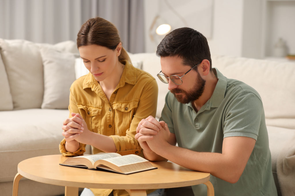 Christian couple praying together over an open Bible at home, growing spiritually in marriage through faith, prayer, and biblical connection.