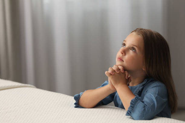Christian child praying with folded hands and looking toward heaven, learning intercessory prayer, faith, empathy, and trusting God to care for the needs of others.