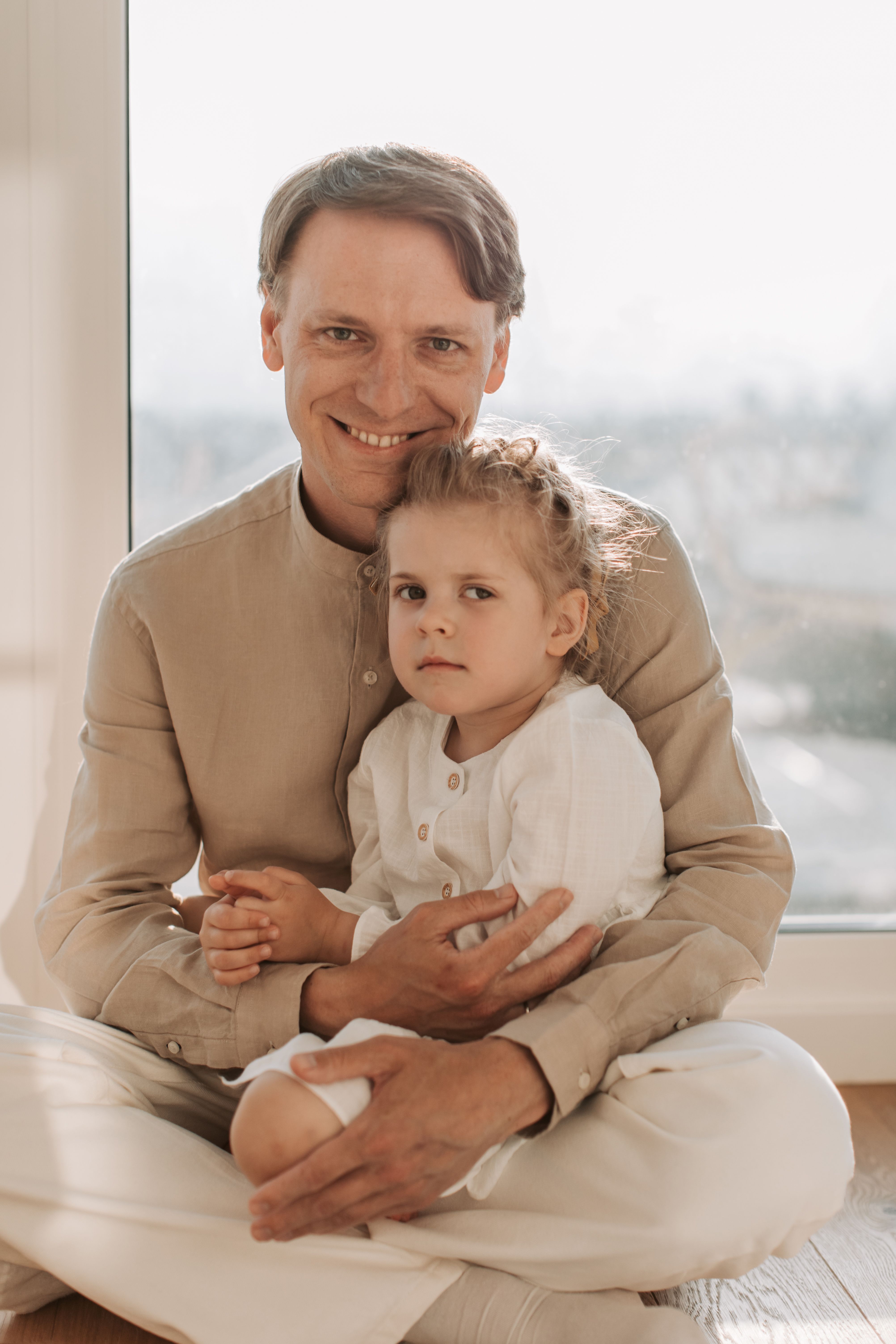 Loving father embracing his young daughter while sitting together at home, showing a close father-daughter bond, affection, emotional security, and the importance of a dad's presence in a child's life.