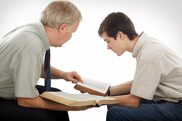 Father reading the Bible with his young son at home, teaching biblical values, Christian faith, responsibility, character, and godly manhood through quality family time.