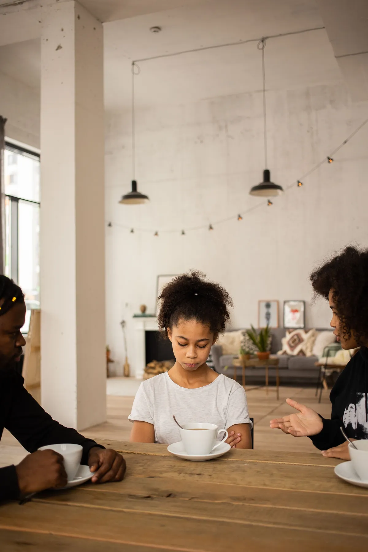 A quiet child sitting between family members at a table while they try to engage her in conversation, illustrating the importance of understanding introverted children, emotional needs, and communication in a busy family.