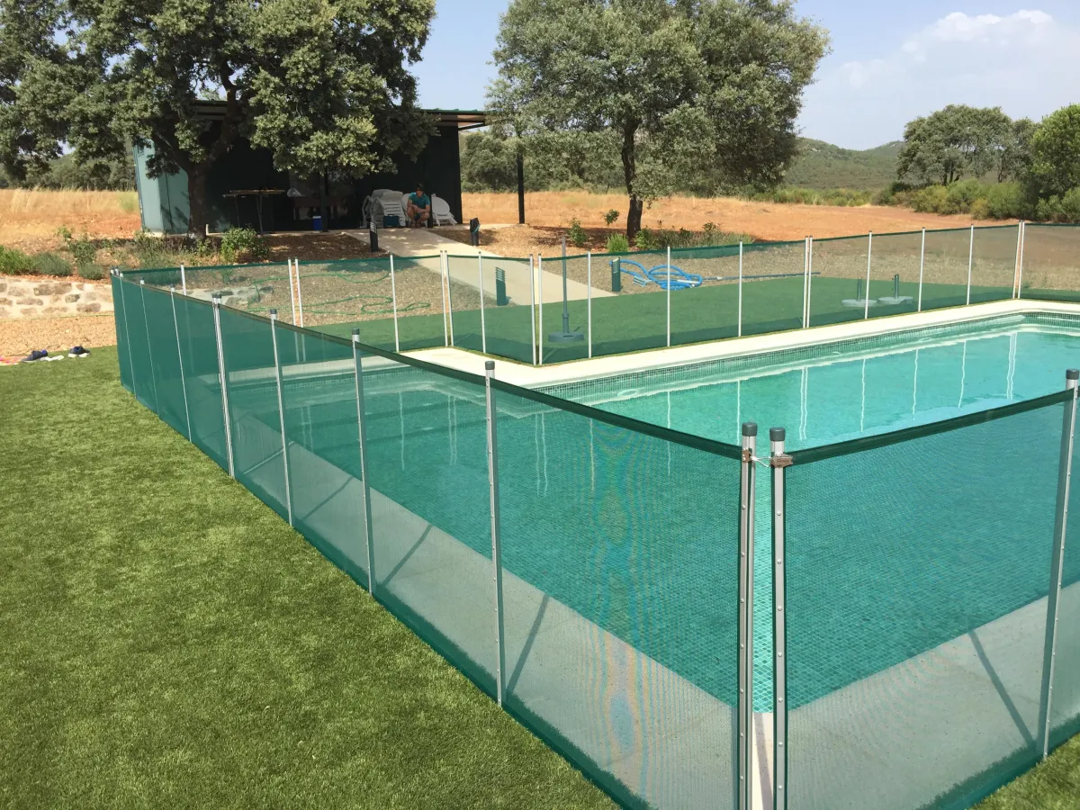 Piscina rodeada de vallas de seguridad verdes Babysecur, perfectamente integradas en un entorno natural con césped y árboles.