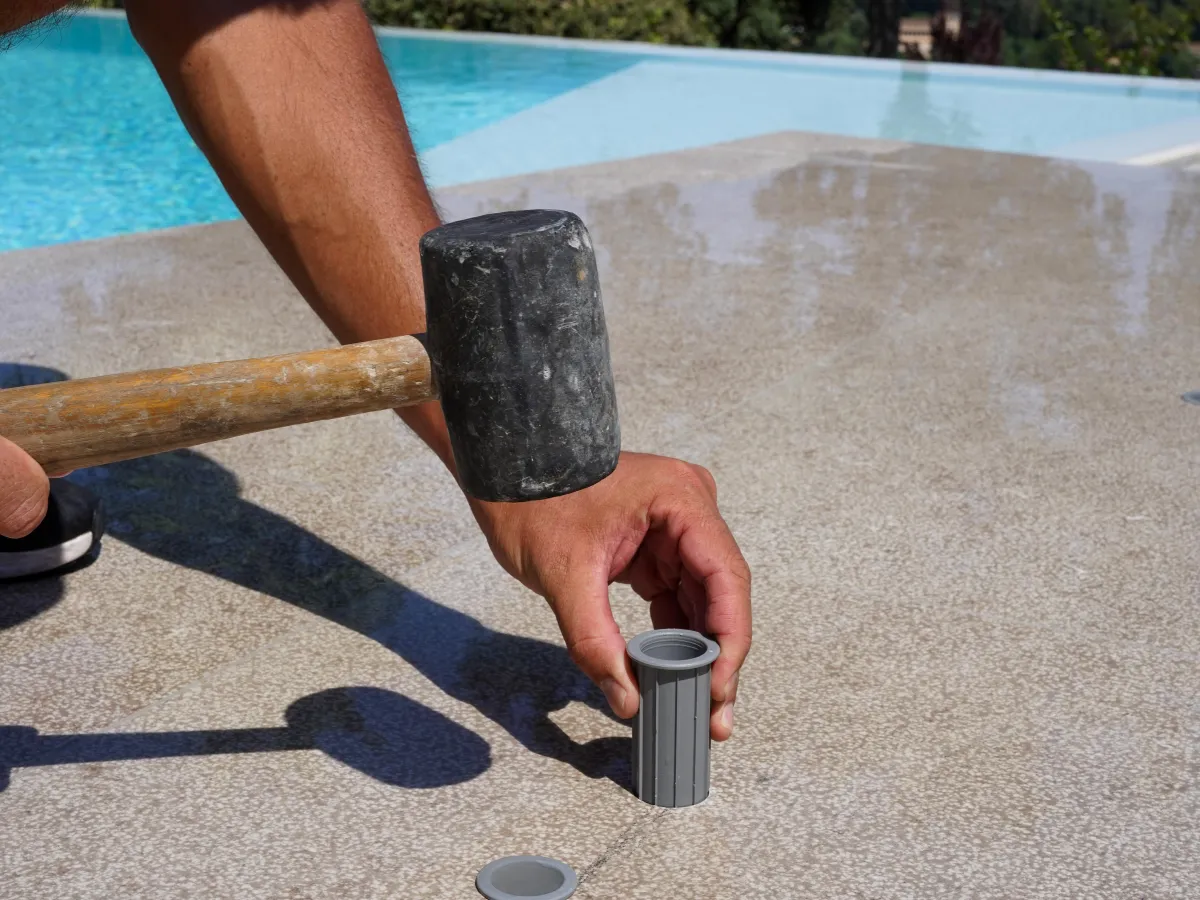  Técnico instalando un anclaje para vallas Babysecur en el suelo con la ayuda de un mazo de goma, garantizando una fijación precisa junto a la piscina.