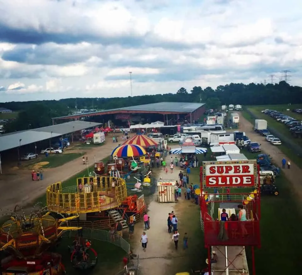 An outdoor fairground bustling with activity, featuring a **Super Slide**, colorful rides, tents, food stalls, and families enjoying the event under a partly cloudy sky. This lively scene highlights the importance of **True Cleaning Experts'** event cleaning services, ensuring a clean and organized environment before, during, and after large gatherings.