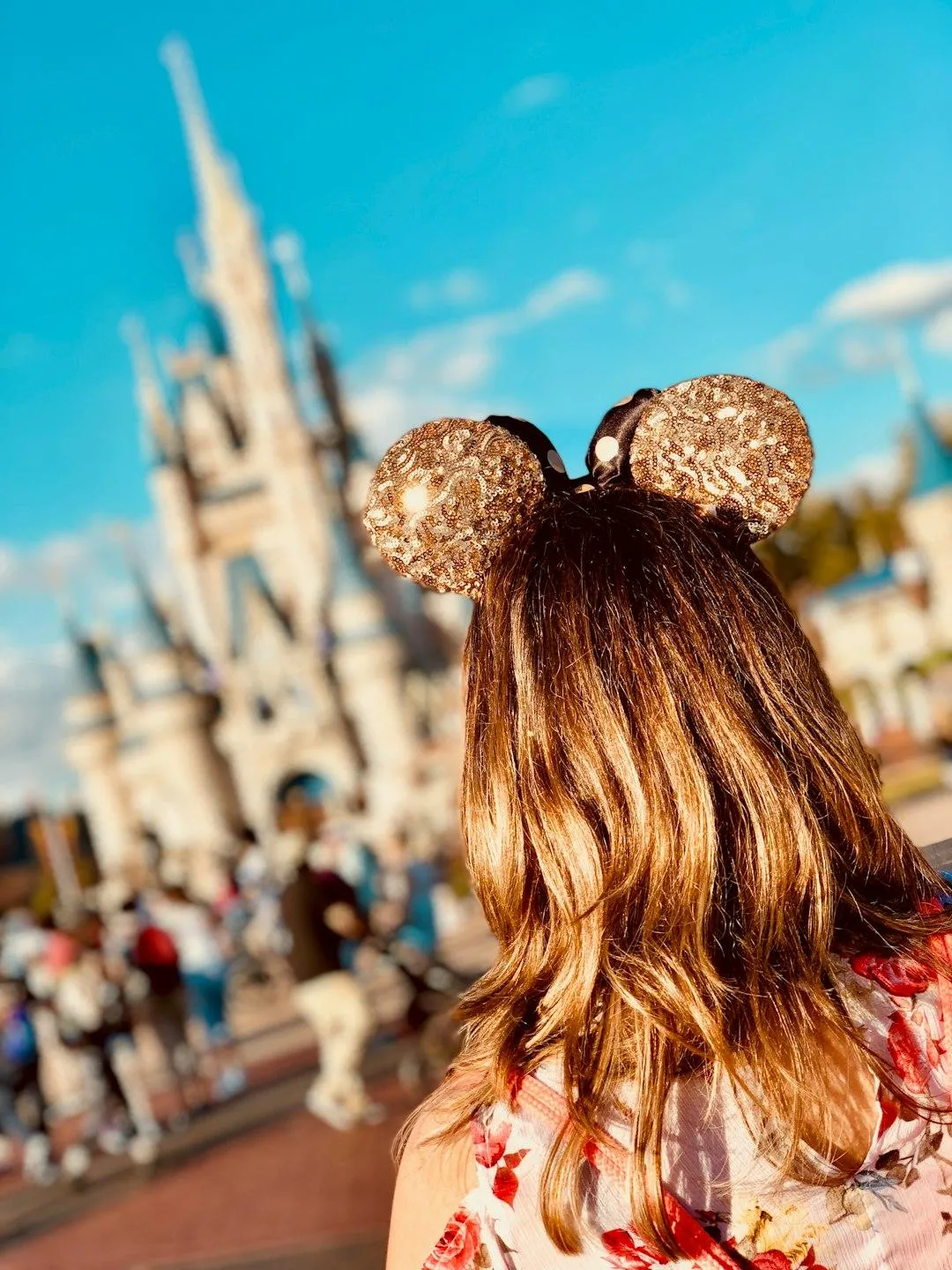 A woman with sparkly Disney ears looking at the Disney castle