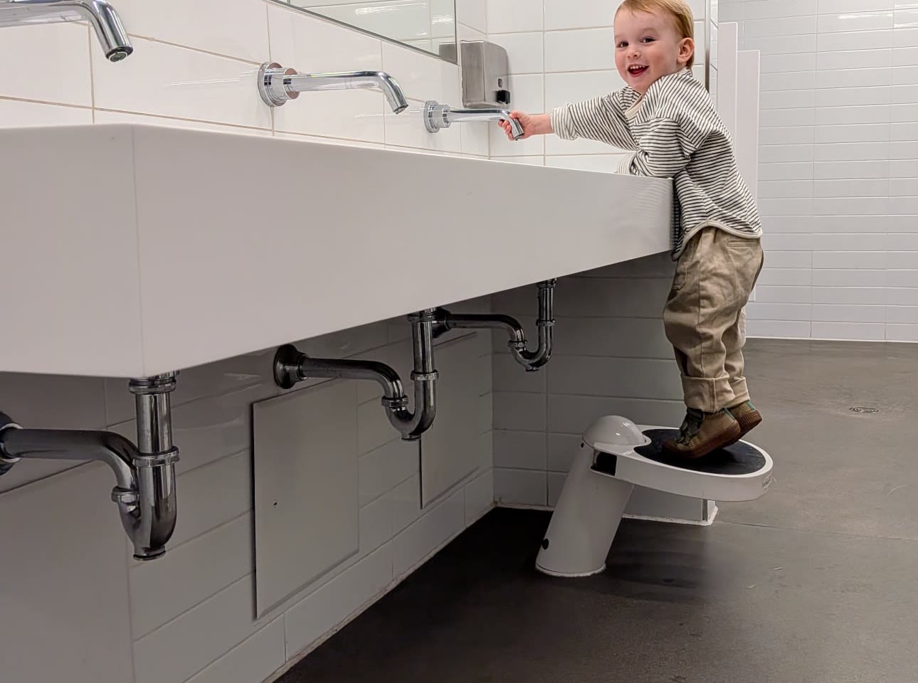 Toddler standing on a Klimbo K01 step stool at a public restroom sink