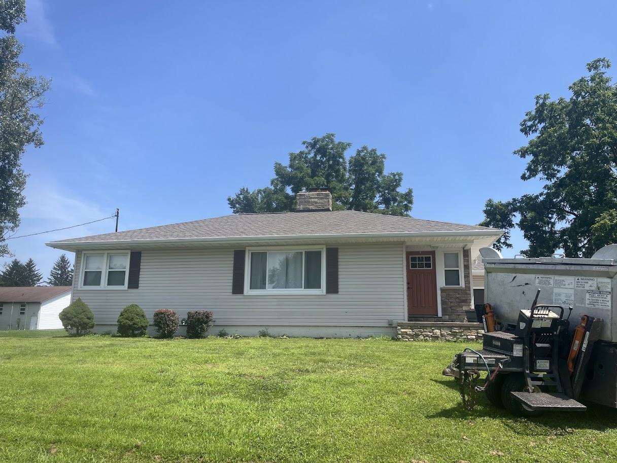Before image of the house with an older, lighter gray/brown roof showing signs of wear.