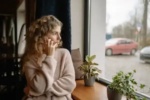 Vrouw staat bij het raam en belt terwijl ze naar buiten kijkt, als beeld voor een partner die zoekt naar houvast en steun naast PTSS thuis.