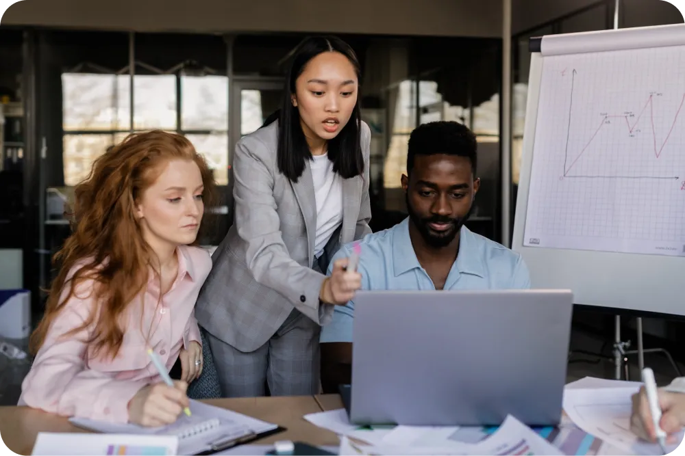 Image of 3 employees gathered around a laptop discussing business growth