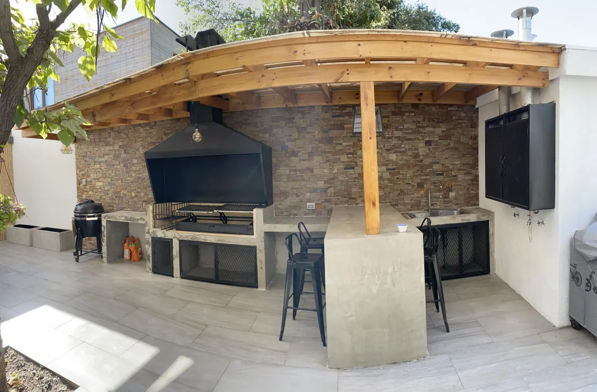 Quincho con pérgola de madera, muro de piedra y parrilla