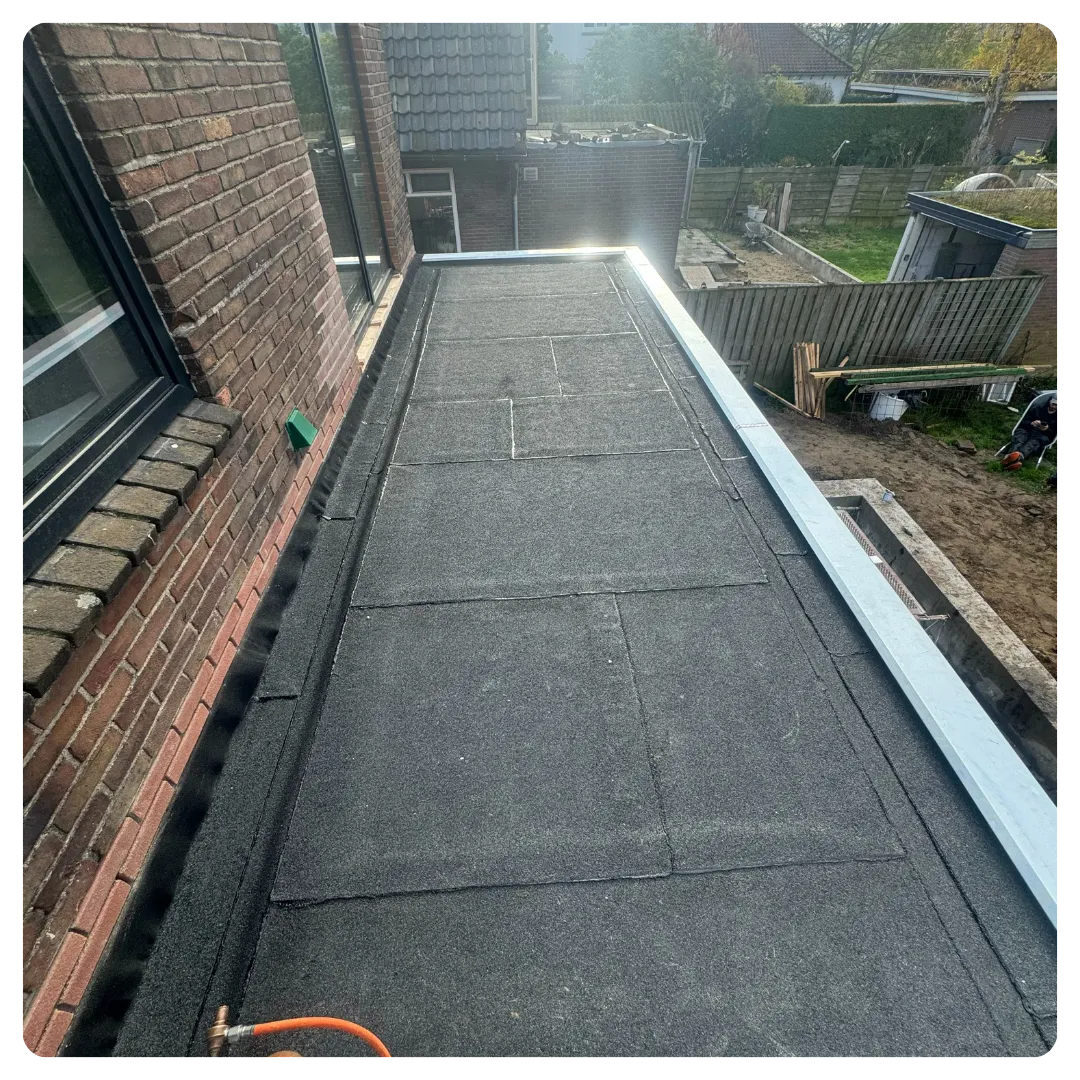 Plat dak met bitumen dakbedekking naast een bakstenen gevel