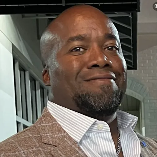 Image of Dr. Boler, the owner of the clinic, smiling warmly. He is an African American man wearing a professional suit. The background is softly blurred, emphasizing his friendly and confident demeanor.