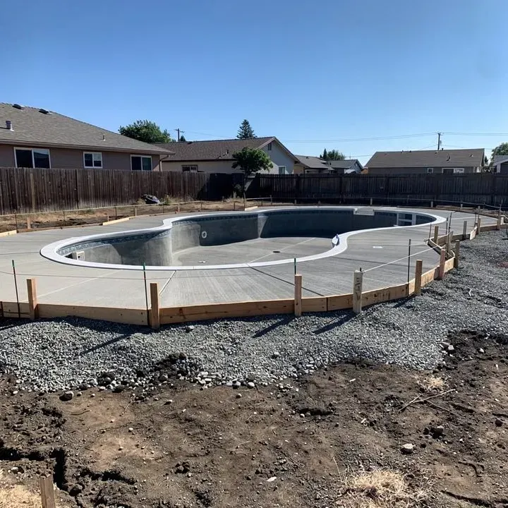 Concrete pool deck in early construction stage with wood forms and gravel subbase around residential pool in Red Bluff California