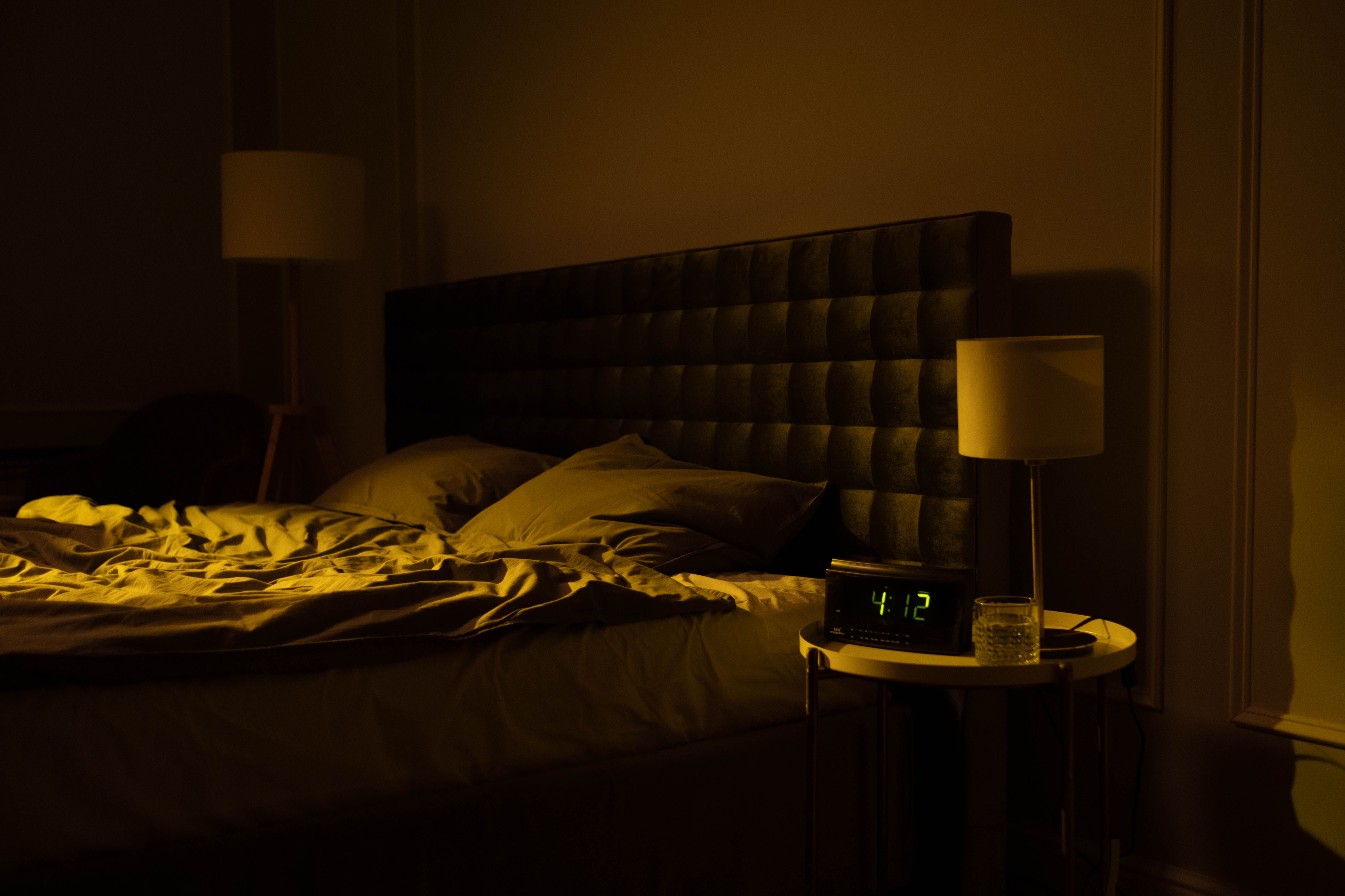 Dimly lit bedroom with an unmade bed and bedside lamp, set for a good night's sleep