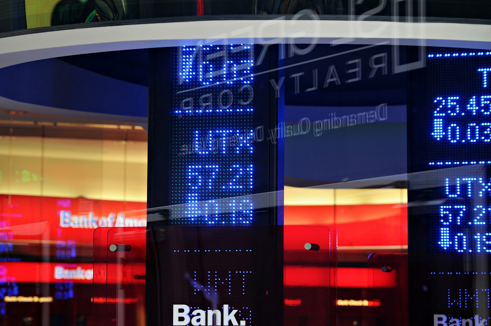 Reflections of stock ticker boards and bank signage on a Wall Street building facade