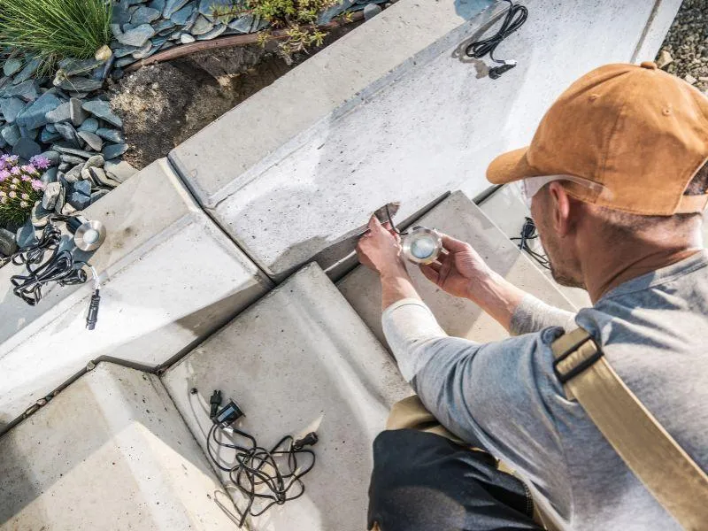 An electrician is installing outdoor LED step lighting along concrete stairs for a residential landscape lighting project in Indianapolis by Branch Electric. Branch Electric performing a custom outdoor lighting installation on concrete steps in Indianapolis. Enhance safety, style, and energy efficiency with expert LED upgrades.