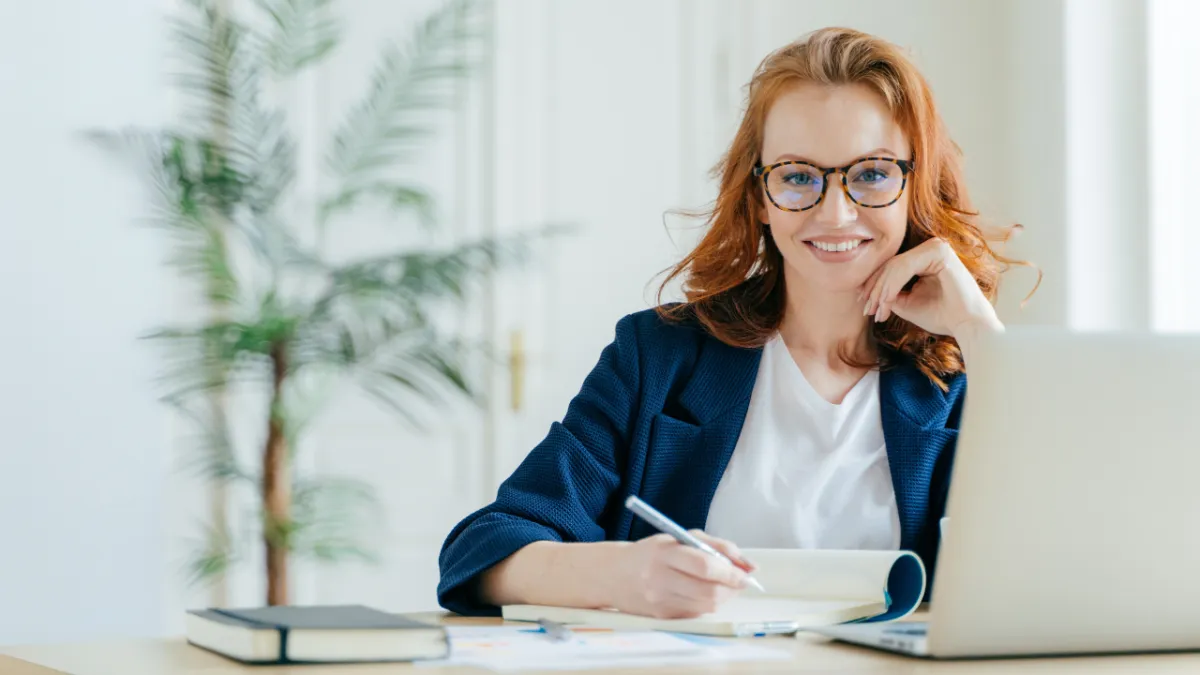 red headed woman in glasses sitting at a desk