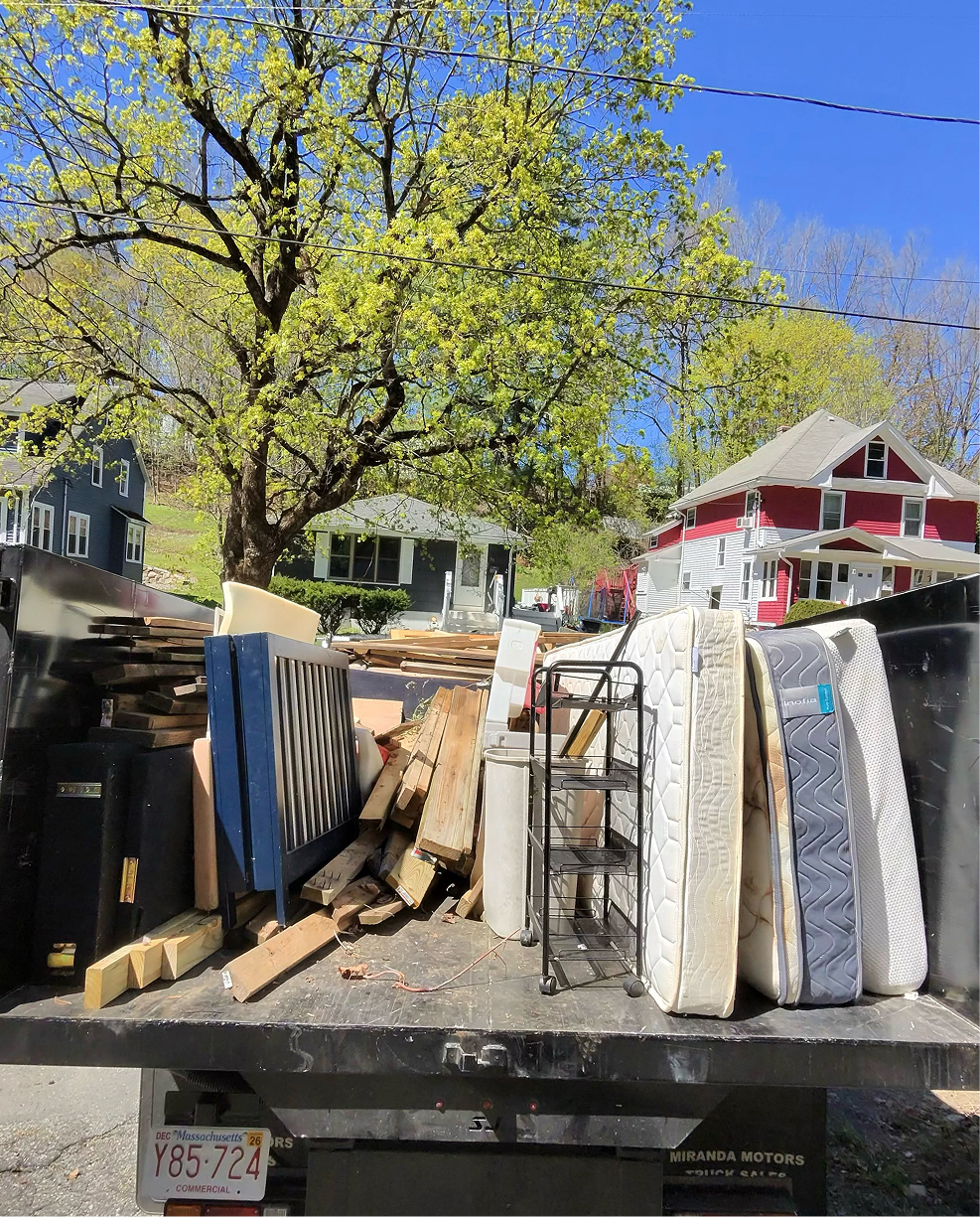 Junk removal truck loaded with a sofa, TV, air conditioner, boxes, and mixed household debris after a full home cleanout