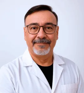 Gabriel Calle reviewing patient notes in a sunlit office, surrounded by medical books and a digital tablet, exuding focus and compassion. The setting is warm and inviting, with natural light highlighting his attentive demeanor and commitment to patient care.
