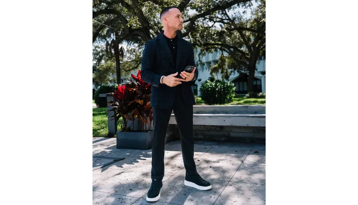 Marc Effron wearing sneakers and a black suit and standing in front of a building.