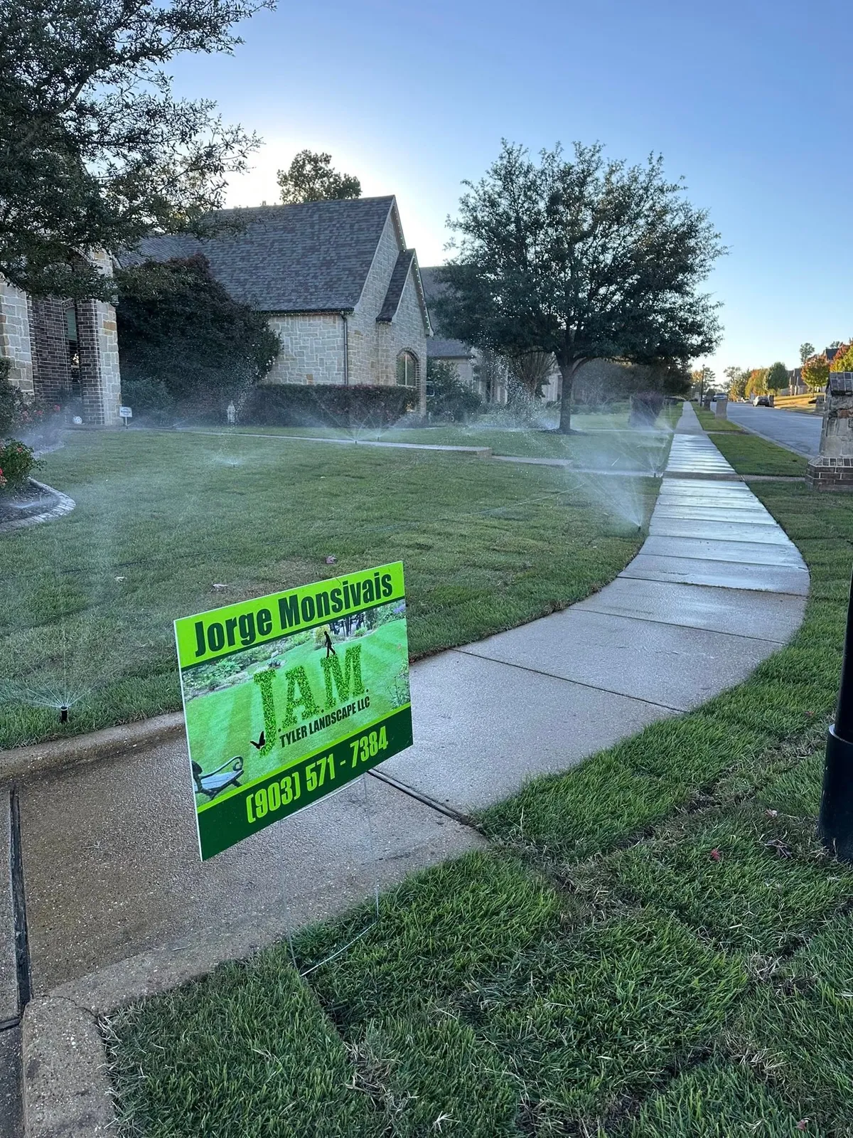 Sprinkler system running across a front lawn with the JAM Tyler Landscape yard sign