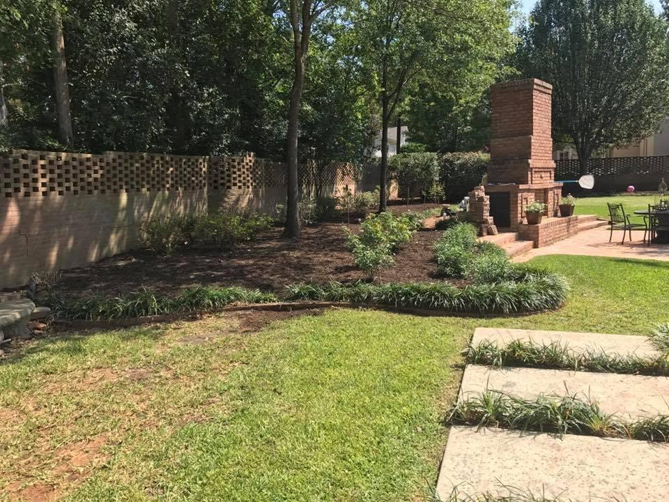 Landscaped planting beds around an outdoor brick fireplace and patio