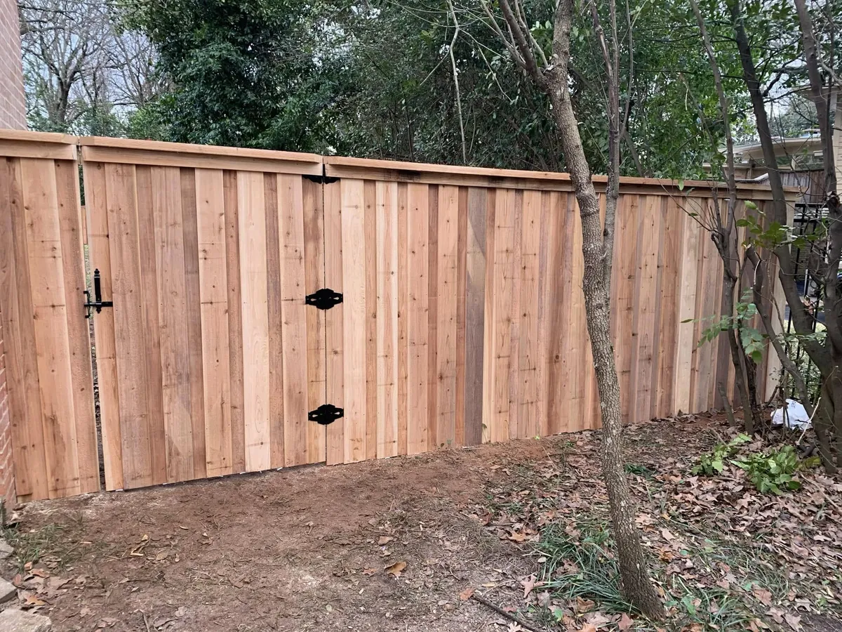 New cedar privacy fence and gate with black hardware in a wooded back yard