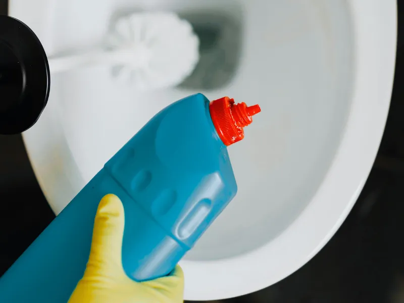 A cleaner holding toilet bowl cleaner with rubber gloves on