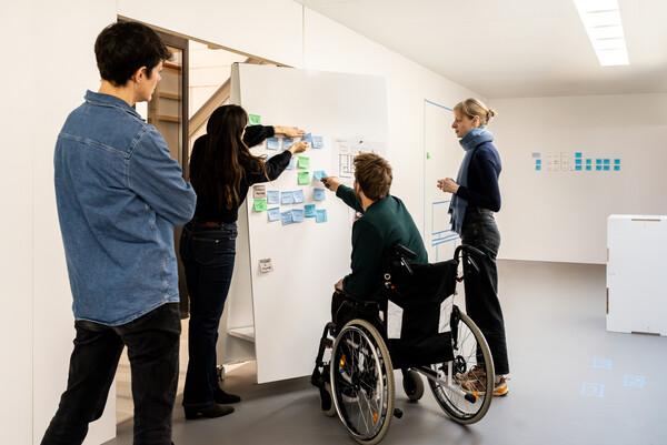 Person using a wheelchair collaborating with colleagues around a whiteboard during an inclusive team brainstorming session.