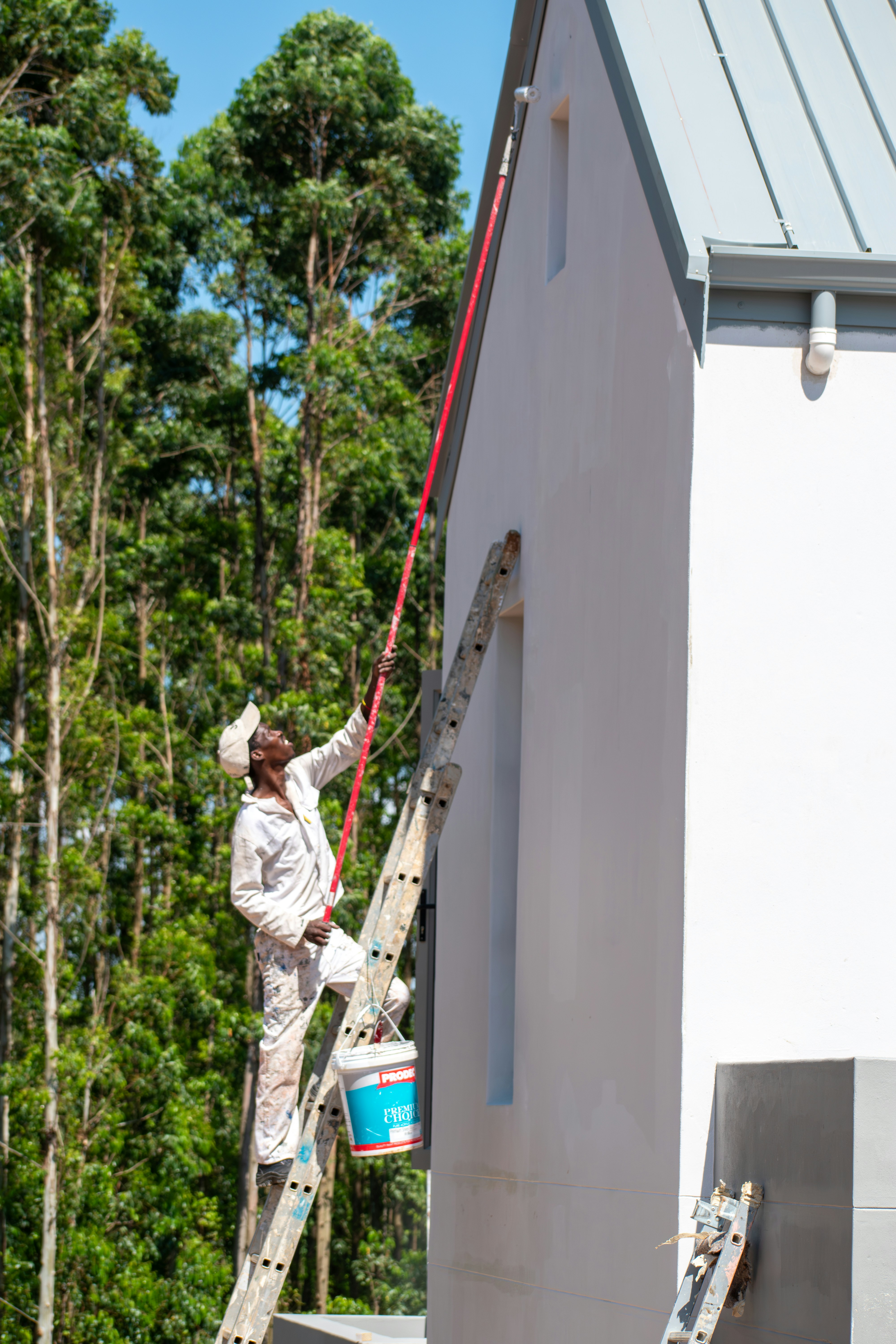 white shirt african man painting wall of house white