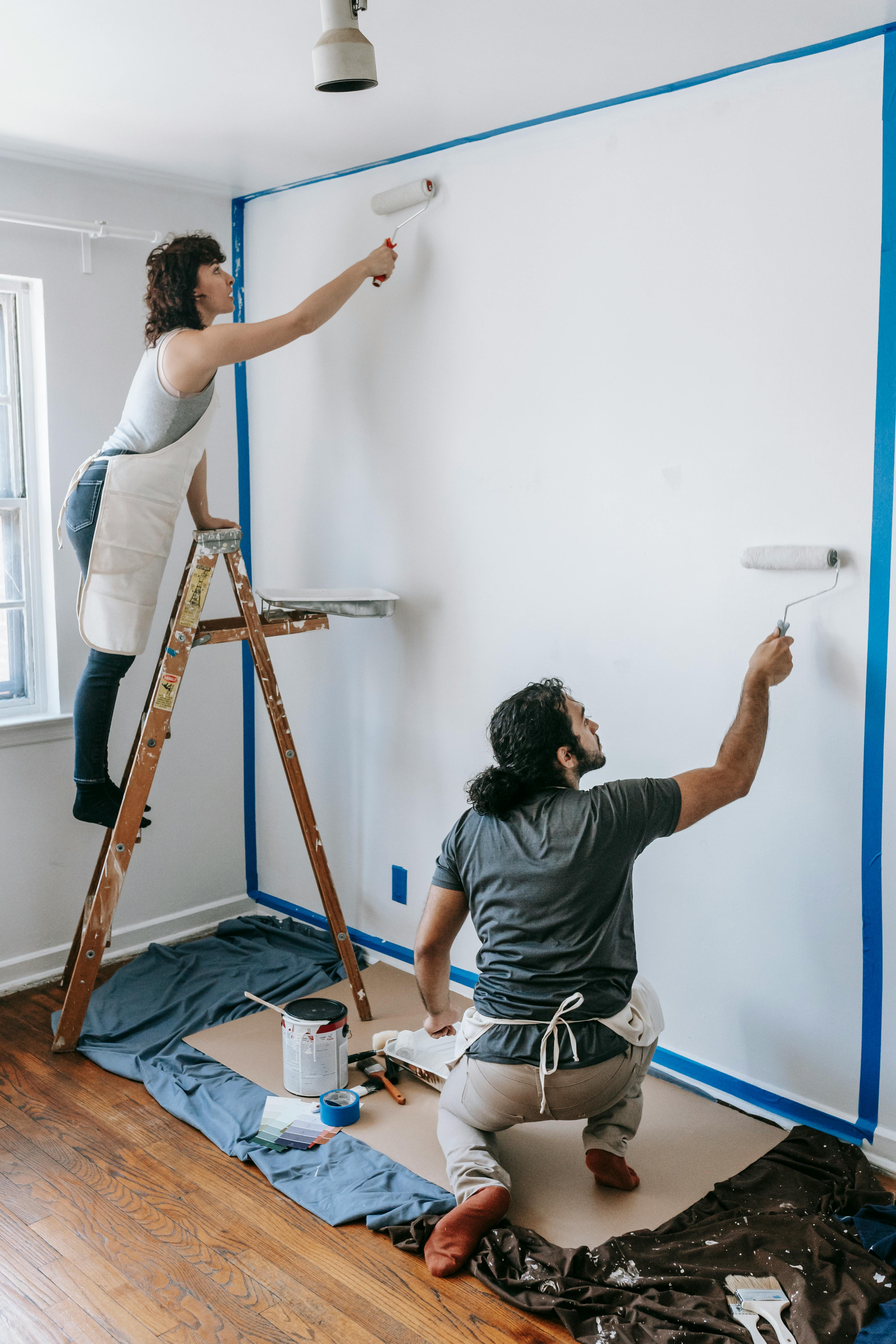 man and woman using paint roller to paint wall white