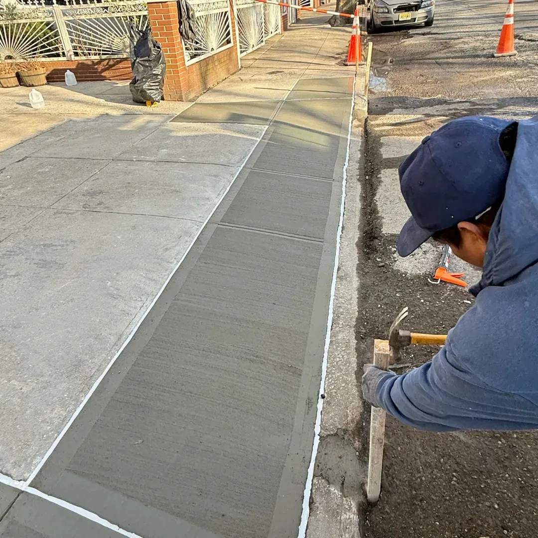 Worker repairing sidewalk with freshly poured concrete in a residential area of Queens, New York.