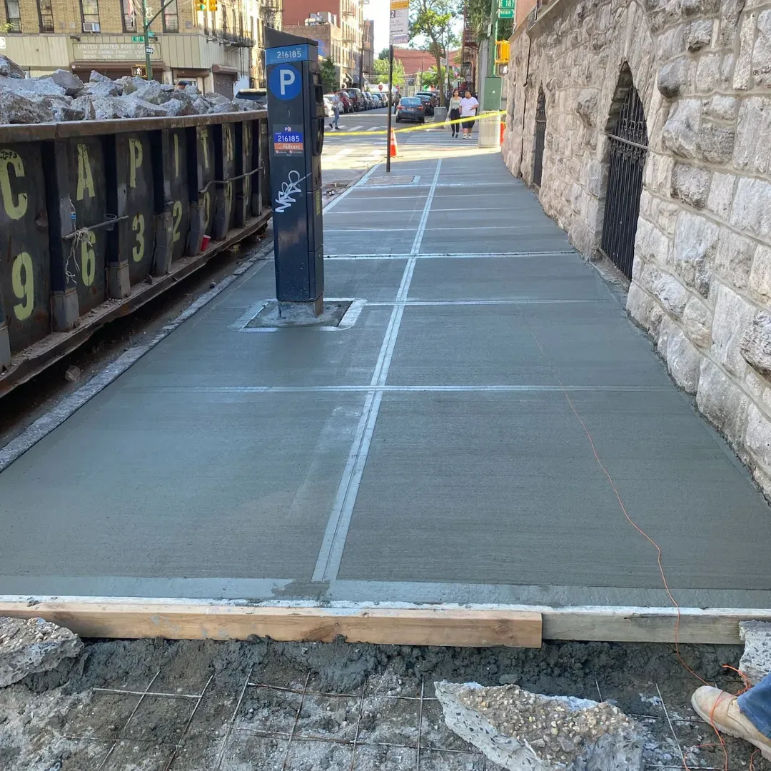 Freshly poured concrete sidewalk in front of a stone building, in an active construction zone in Queens, New York.
