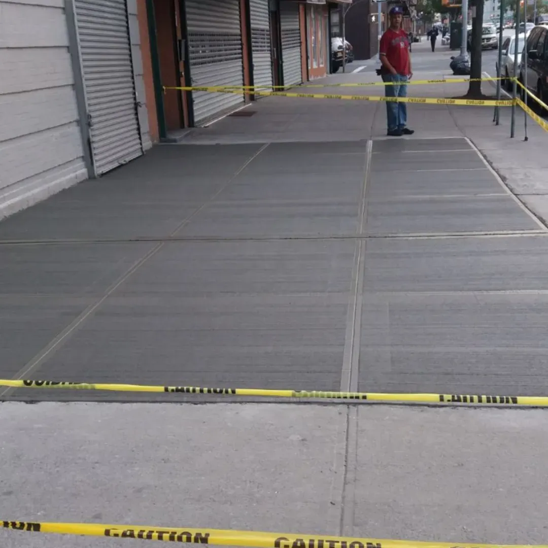 Fresh concrete sidewalk with a clean finish and caution tape in front of local businesses in Queens, New York.