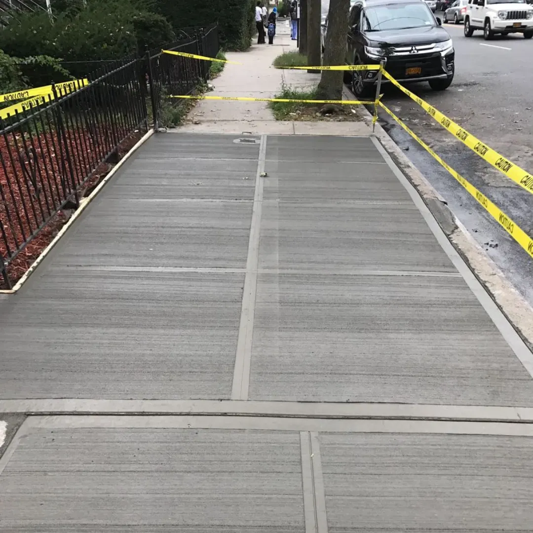 Freshly poured concrete sidewalk with clean finish and caution tape in a residential area of Queens, New York.