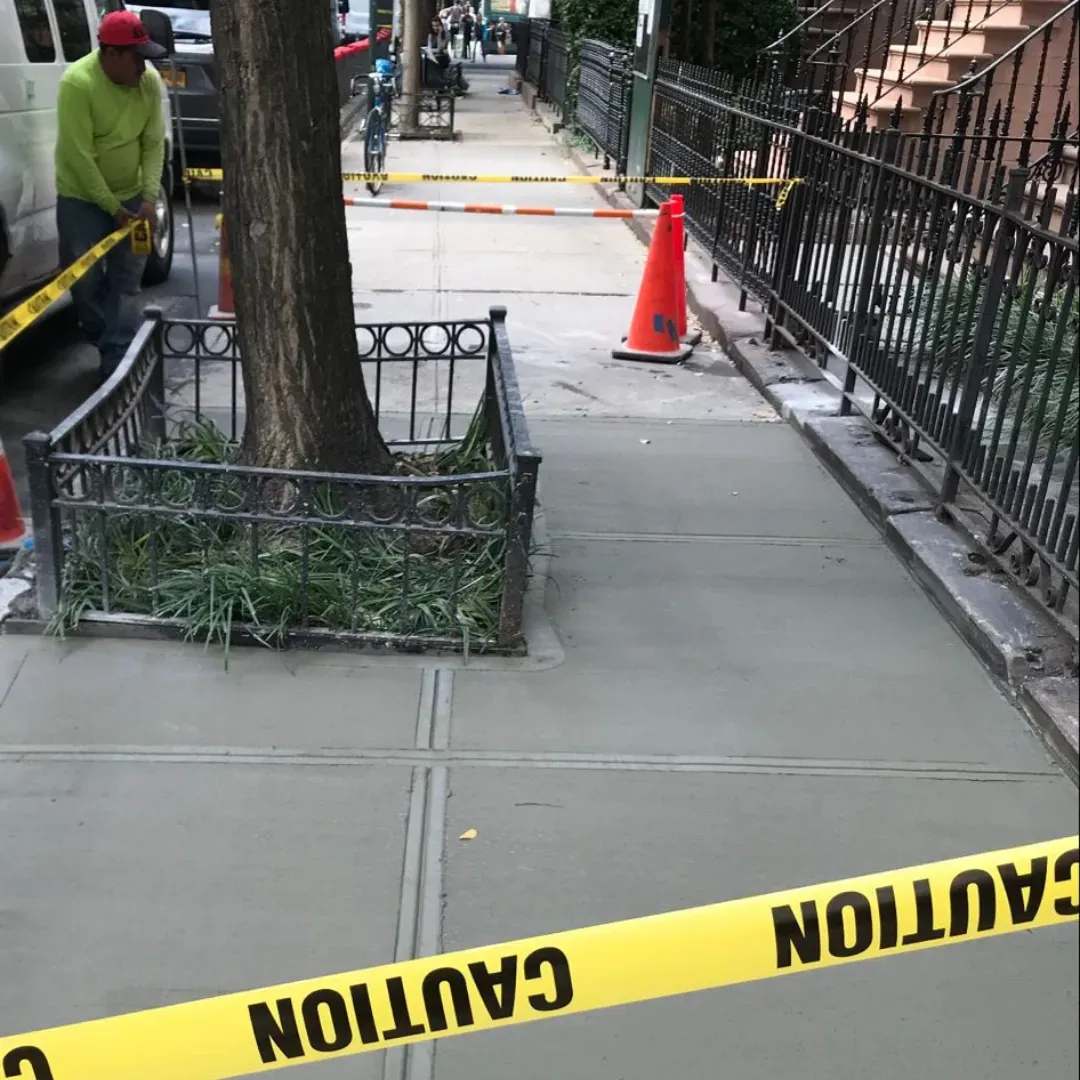 Repaired concrete sidewalk with caution tape in urban setting.