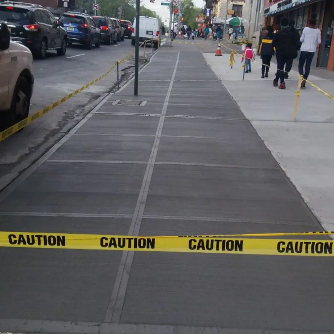 New concrete sidewalk with caution tape on a street in Queens, New York.