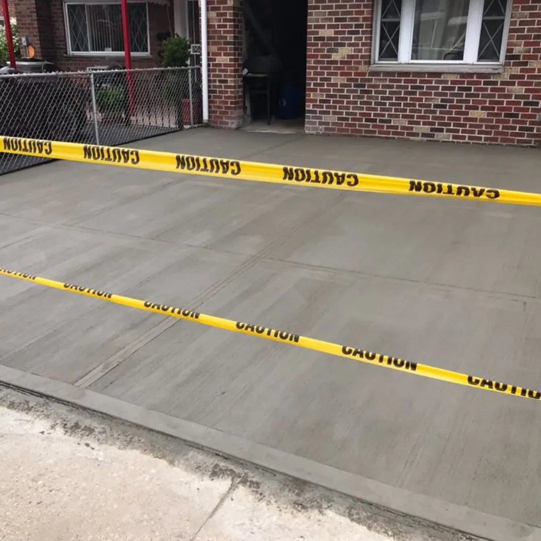 New concrete driveway with yellow caution tape at a residential property in Queens, New York.