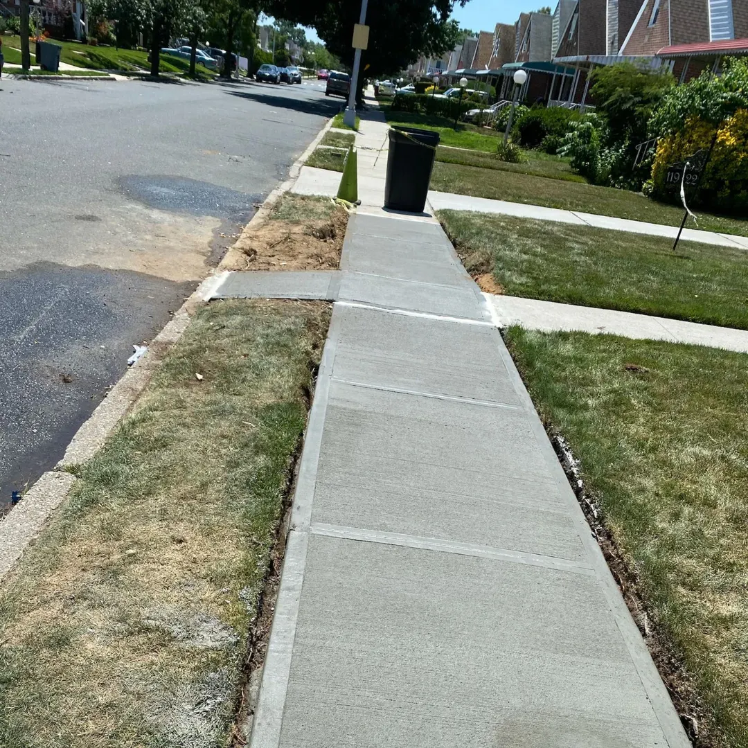 New concrete sidewalk in a Queens, New York neighborhood, with a trash can in the background.