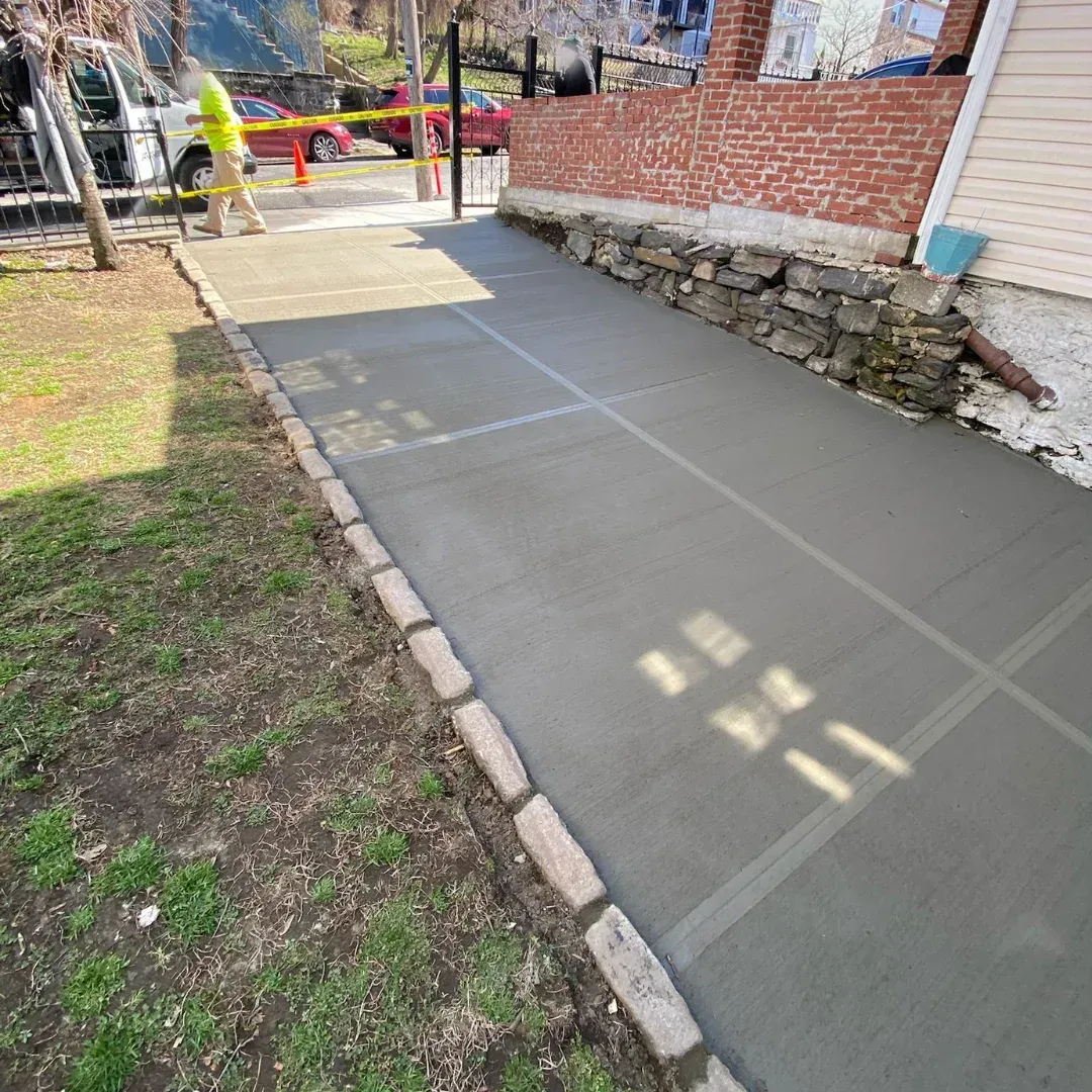 Concrete driveway with stone curb at a Queens, New York residence; worker and caution tape.