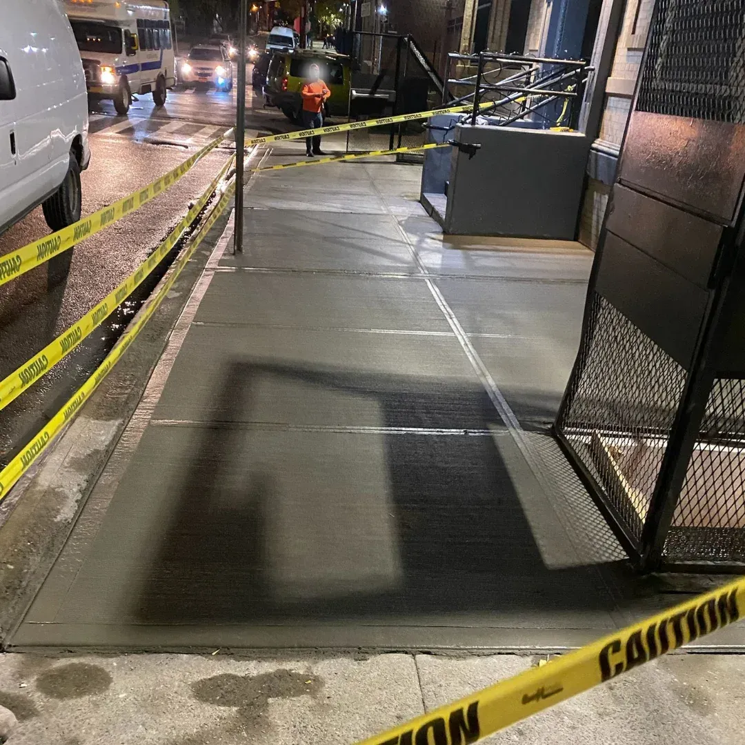 In Queens, New York, a newly repaired concrete sidewalk is seen at night, marked off with yellow caution tape.