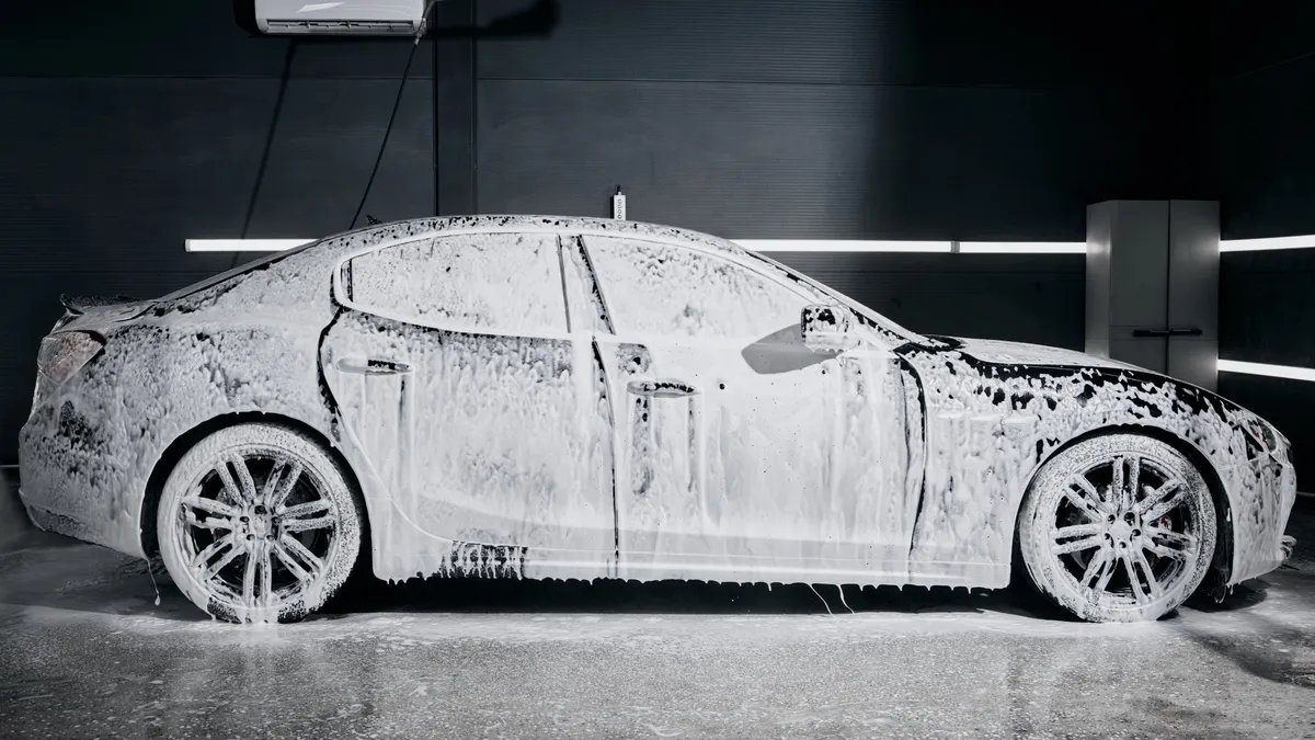 Black luxury sedan covered in snow foam during a hand car wash