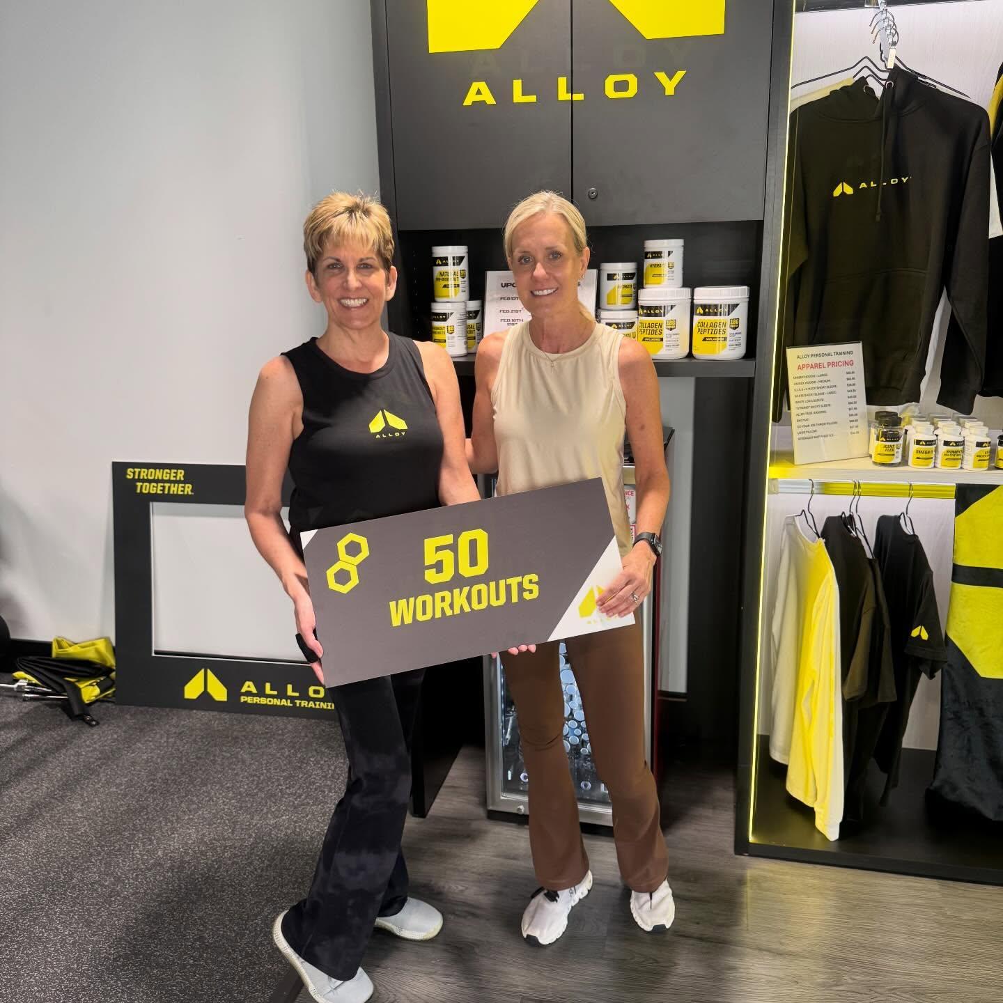 Two women celebrating their 50th workout milestone at Alloy Personal Training South Tampa during a small group fitness session. Focused on strength training, mobility, and consistency for adults over 40.