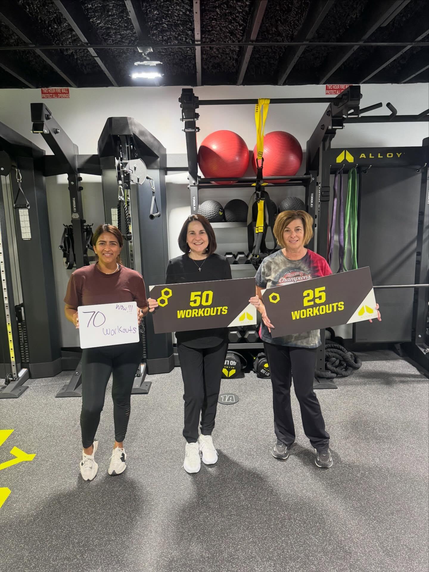 Three adult women celebrating 25, 50, and 70 workout milestones at Alloy Personal Training South Tampa during small group fitness training focused on strength training, accountability, and safe personal training for adults over 40.