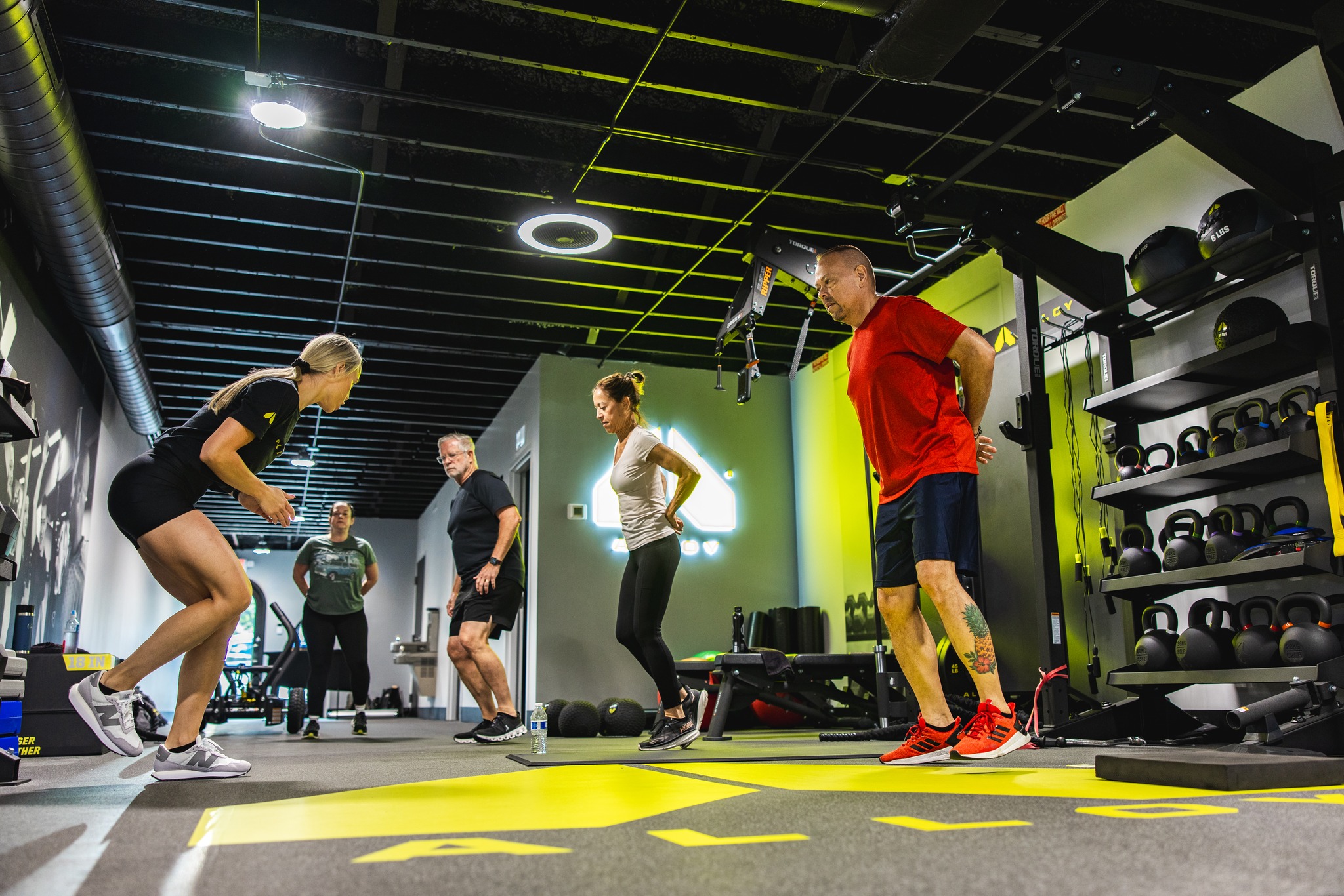 Participants in a small group functional fitness class at Alloy Personal Training South Tampa performing a variety of exercises, including strength training and cardio, guided by a certified trainer. Focused on building strength, balance, and mobility for adults over 40.