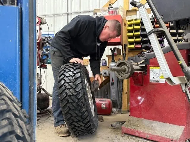 An automotive technician working on a large all-terrain vehicle tire using a professional shop machine