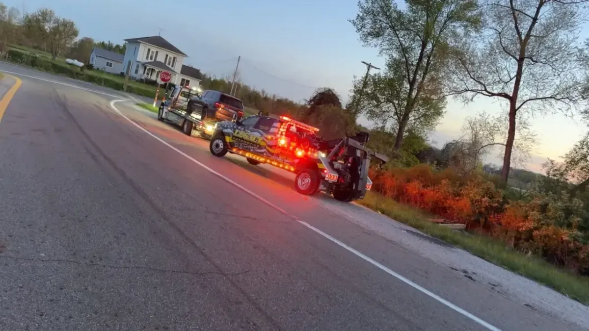 Legacy Automotive tow truck towing a vehicle on a winding two-lane road during sunset
